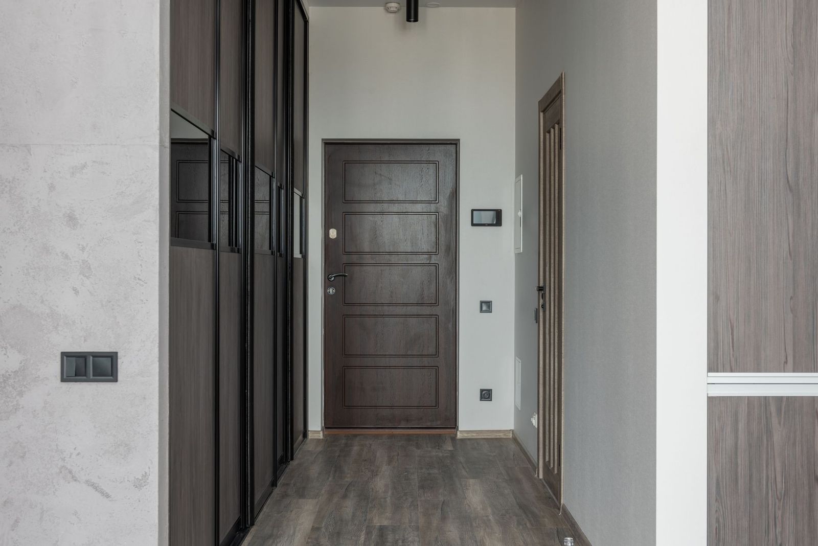 The entry hall of an apartment with a dark front door and closet doors