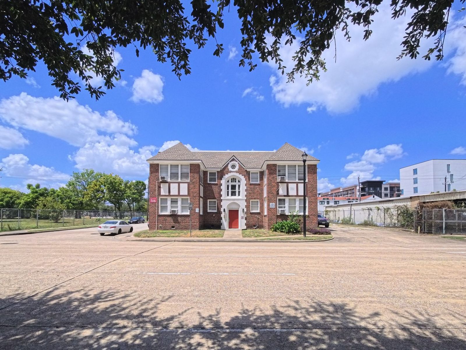 An older three-story brick walk-up apartment building behind an open parking lot