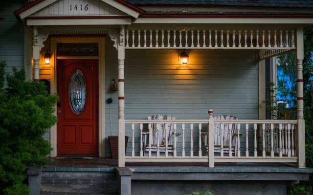 The front porch of an older wood-frame house with lanterns lit and rocking chairs