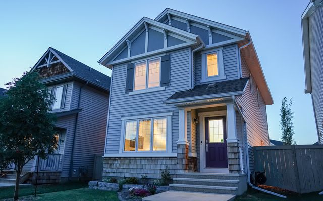 A two-story house with lit windows on a quiet suburban street at dusk