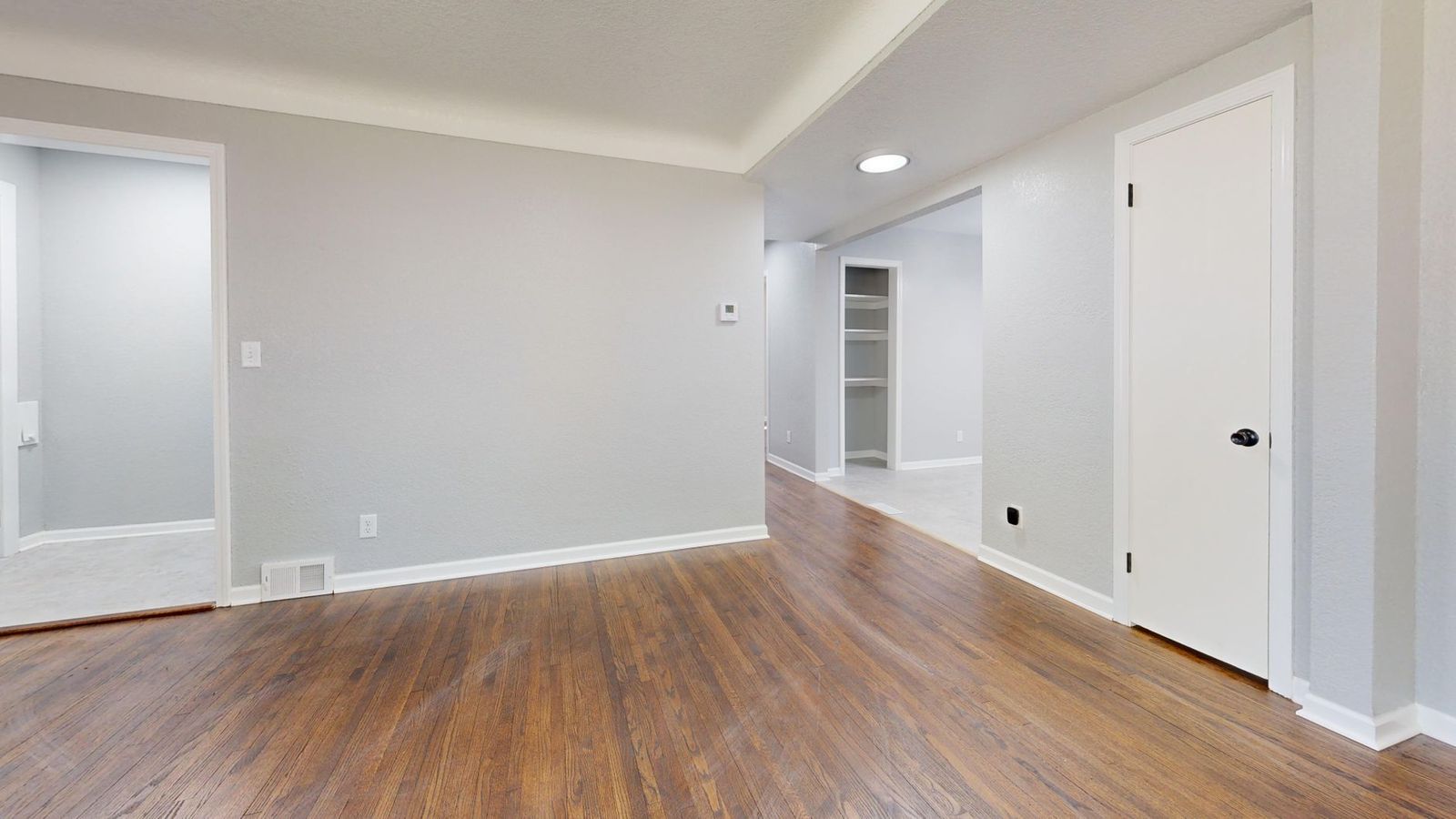 An empty apartment room with hardwood floors, a closet and a white door