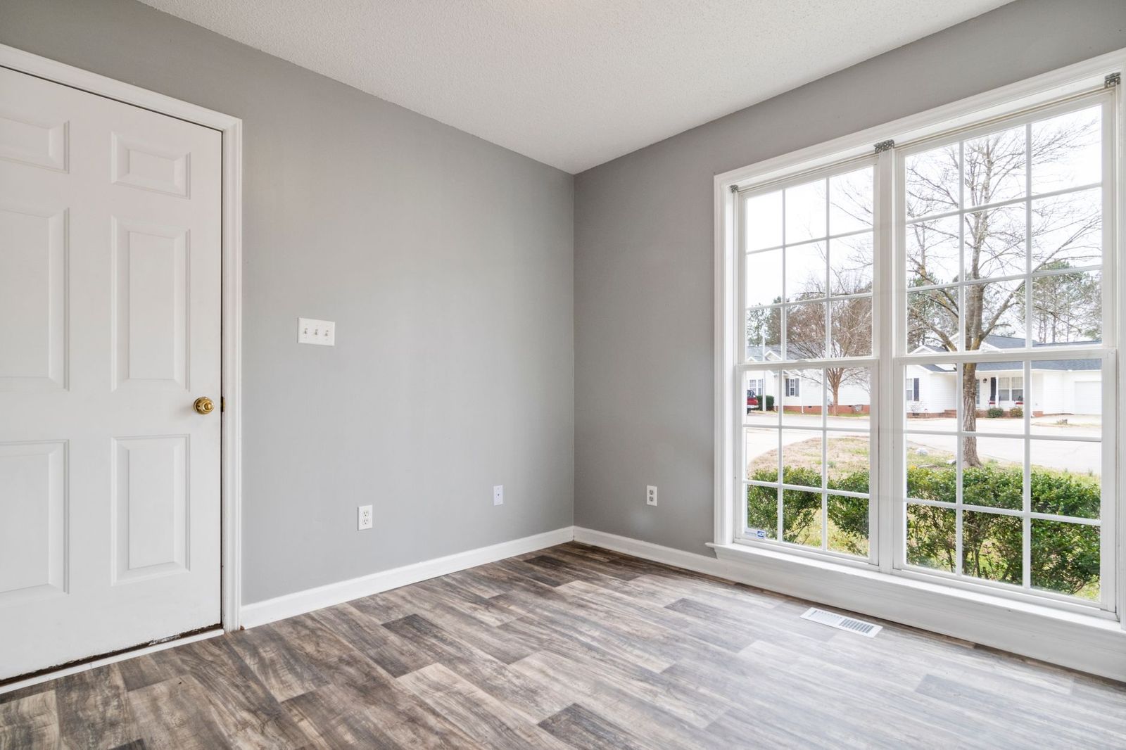 An empty room with a wide window looking onto a street of single-story houses