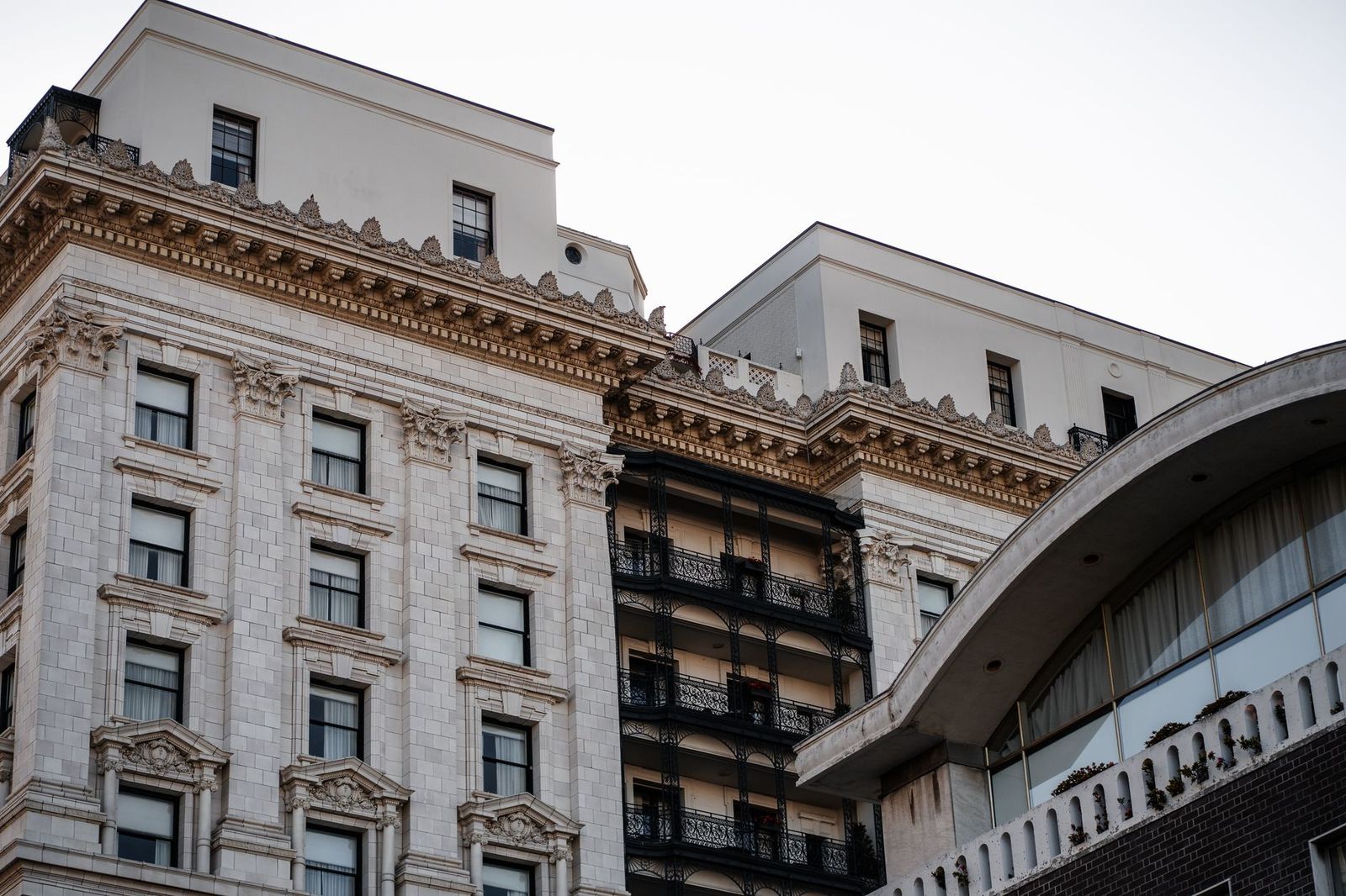 An ornate historic downtown building with iron balconies beside a modern canopy