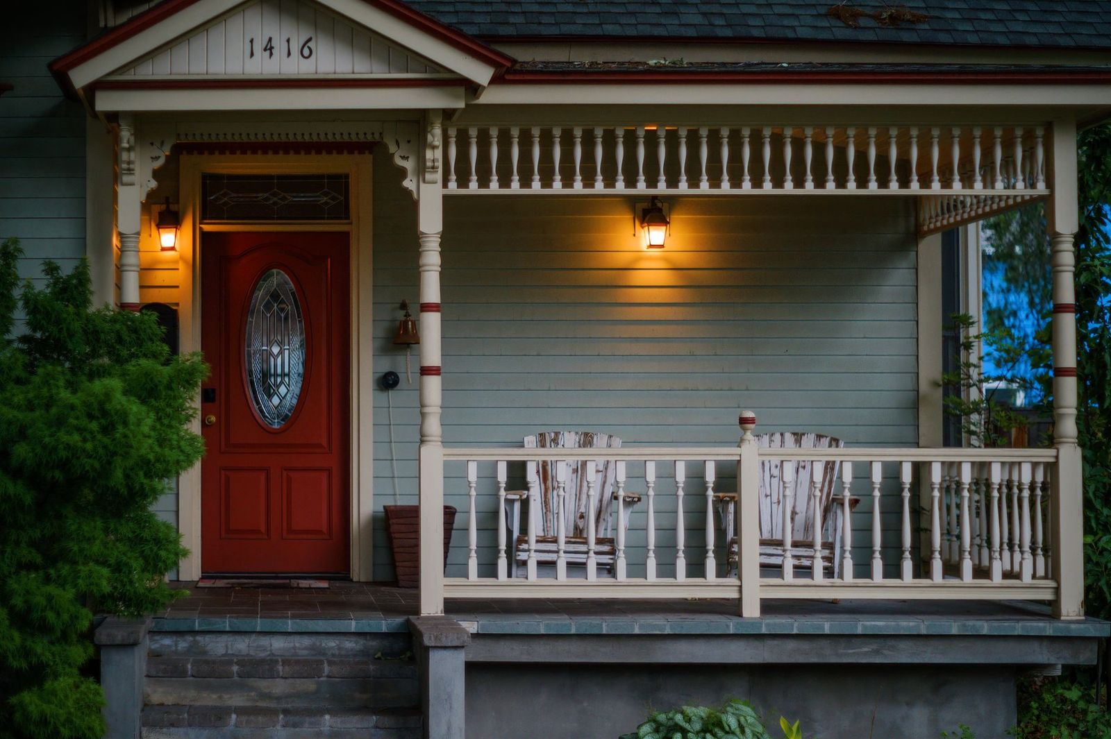 The front porch of an older wood-frame house with lanterns lit and rocking chairs