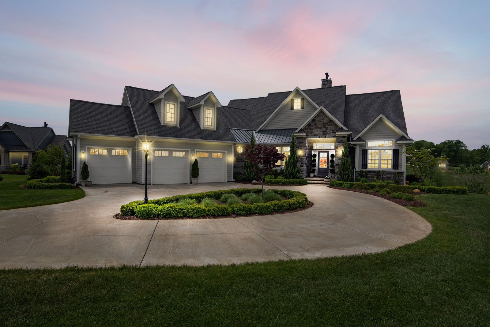A large suburban house with a circular driveway lit at dusk