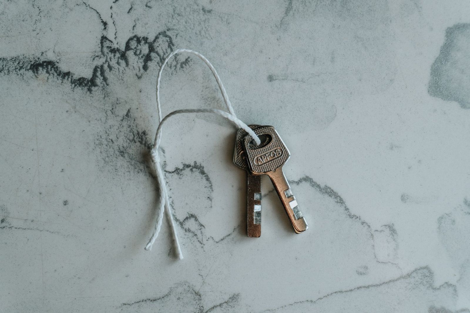 Two apartment keys on a string resting on a pale stone surface