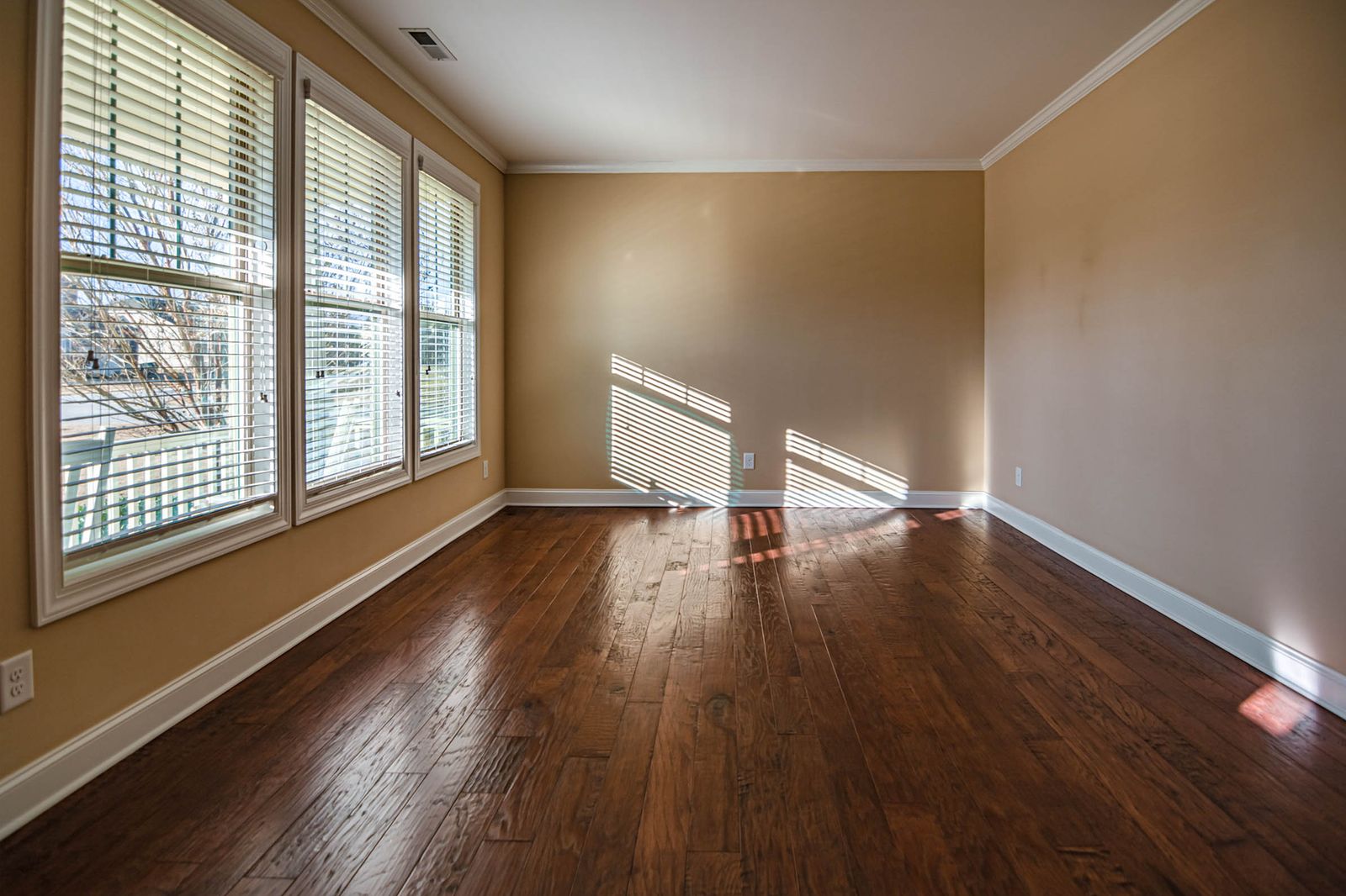 An empty living room with hardwood floors and daylight through slatted blinds