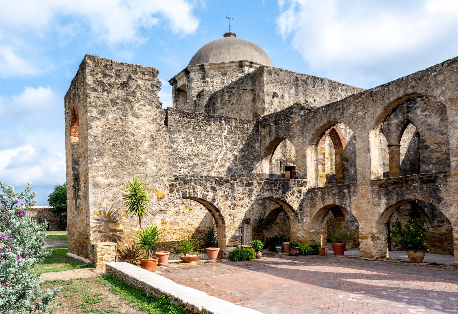 Arched stone walls and potted plants in the convento courtyard of a San Antonio mission