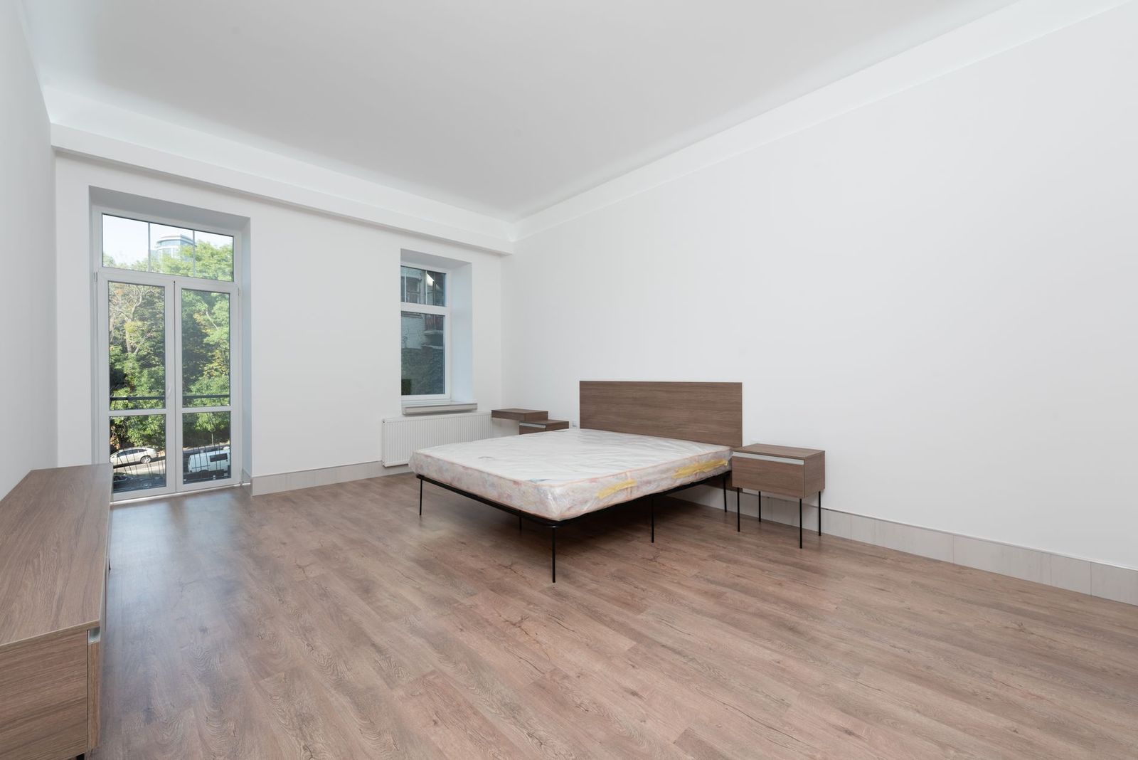 A bare room with a bed frame, mattress and a balcony door