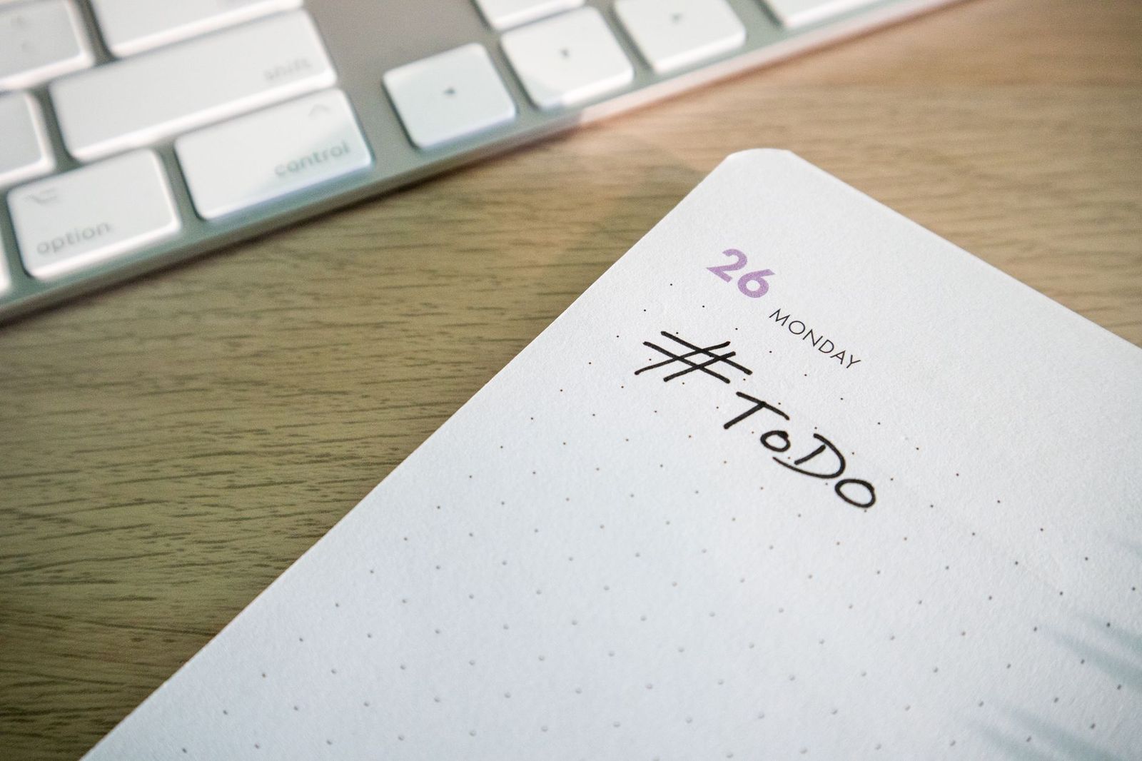 An open dotted notebook on a wooden desk beside a keyboard